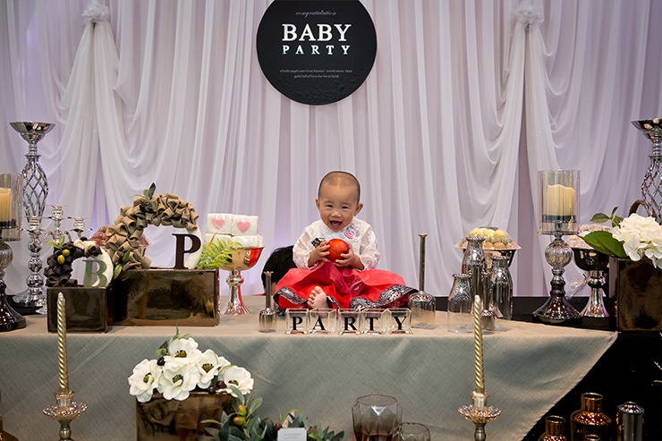 돌잔치 상차림 앞 단독컷 — BABY PARTY 배경, 빨간 한복의 이보은이 과일 들고 웃음