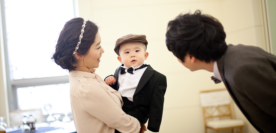 창가에서 엄마가 아이 안고 아빠가 고개 숙여 눈맞춤하는 장면