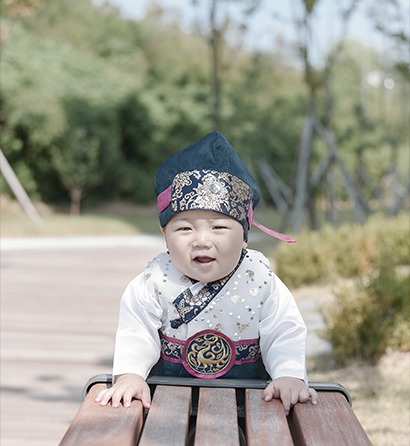 야외 벤치 아이 단독 클로즈업 돌스냅 — 카메라 향해 웃는 표정